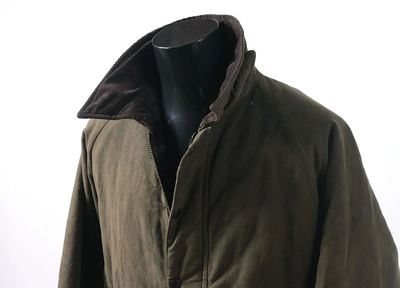 Veste Barbour olive sur mannequin (modèle Endurance) : col en velours côtelé, doublure tartan, zip et pressions — la grammaire commune à la Bedale